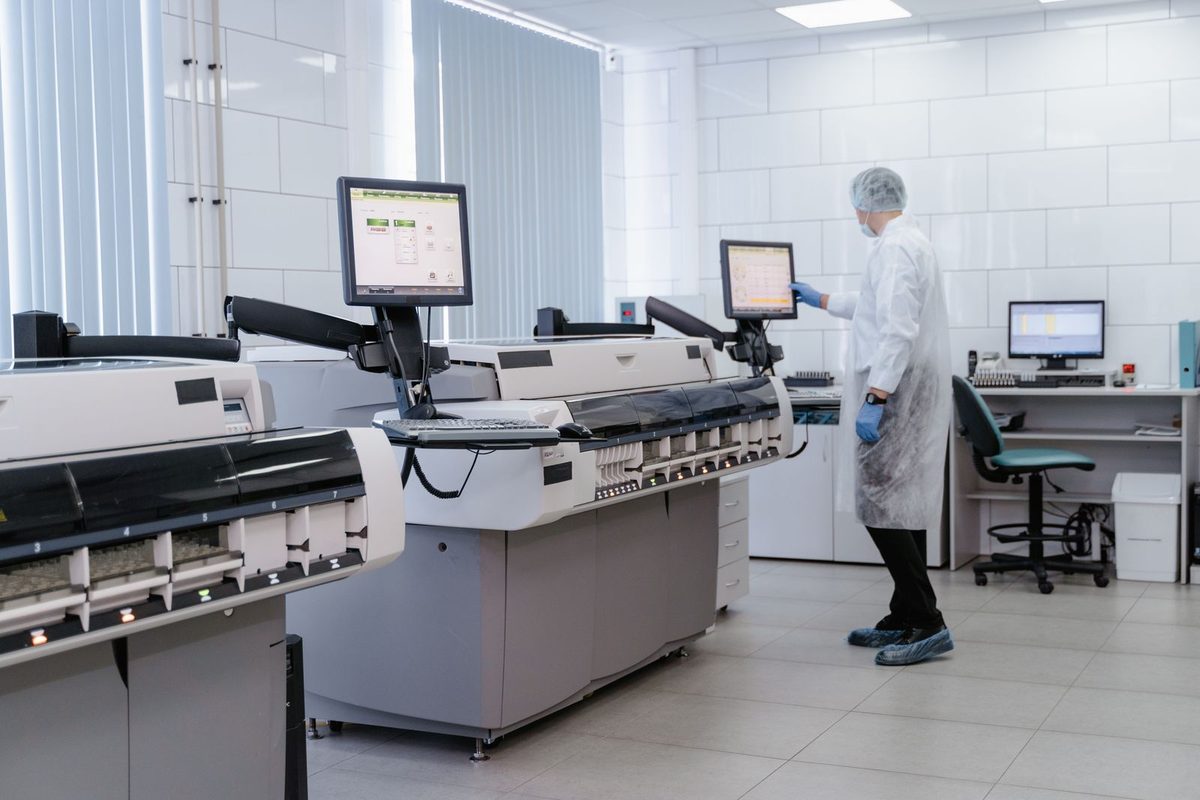 Clinical laboratory with automated analyzers and a technologist at an LIS workstation, the kind of lab that runs moderate- and high-complexity testing